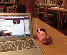 an open laptop computer sitting on top of a wooden table next to a pink purse