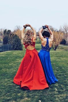 two women in red and blue dresses standing on the grass with their backs to each other