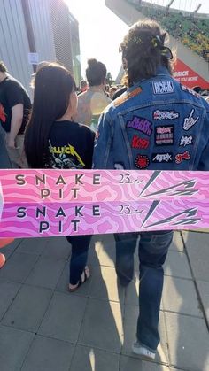 a man holding a pink skateboard with stickers on it while walking down a sidewalk