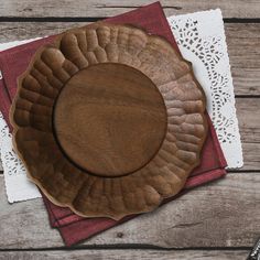 a wooden plate sitting on top of a red and white place mat next to a doily