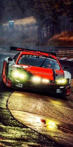 a red and black race car driving on a wet road at night with headlights on