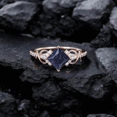 a gold ring with a blue stone surrounded by white diamonds on top of black rocks