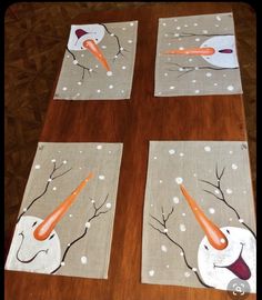 four pieces of paper with snowmen and carrots painted on them sitting on a wooden table