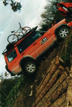 a red truck with a bike on top of it's roof is jumping over a cliff