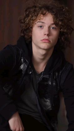 a young man with curly hair wearing a black jacket