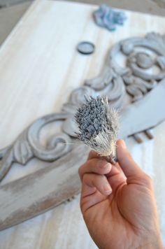 a person holding a brush in front of a carved wooden design on a table top