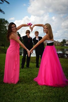 two girls in pink dresses holding hands with three other people standing behind them, all wearing tuxedos