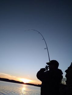 a man is fishing on the water at sunset