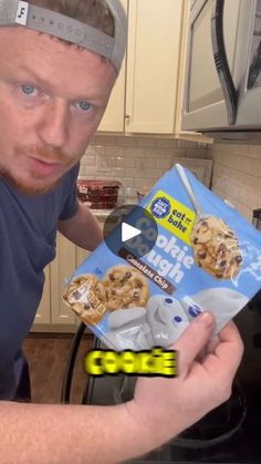 a man holding up a box of cookies in his kitchen with an ad on it