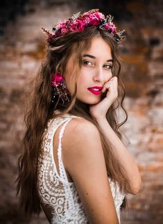 a woman with long brown hair wearing a pink flowered headpiece and holding her hand to her face