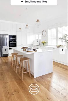 a white kitchen with wooden floors and stools next to an island in the middle