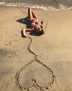 a woman laying on top of a sandy beach next to the ocean drawing in the sand