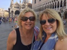 two women standing next to each other in front of a building with many people on it