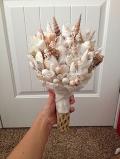 someone holding a bouquet of seashells in front of a door with a hand