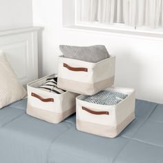 three storage bins sitting on top of a bed next to two pillows and a pillow