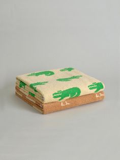 two towels with green alligators on them sitting next to each other in front of a gray background