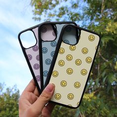 three cases with smiley faces on them are held up in front of some trees and blue sky