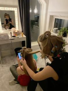 a woman sitting in front of a mirror while blow drying her hair and another person taking a photo