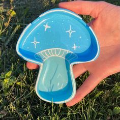 a hand is holding a blue and white mushroom shaped object in the middle of grass