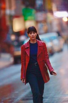 a woman is walking down the street with her hand in her pocket and wearing a red jacket