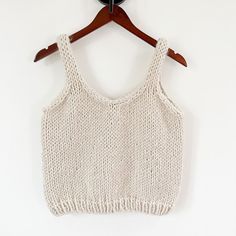 a white knitted tank top hanging on a wooden hanger against a white wall