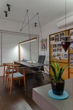 an office with a desk, chair and plant in the middle of the room that has pictures on the wall