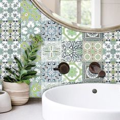 a white sink sitting under a mirror next to a green tiled bathroom wall with potted plants