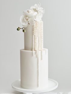 a three tiered white cake with flowers and pearls on the top, sitting on a plate