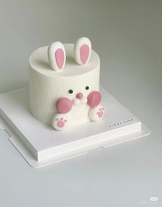 a cake with white frosting and pink ears sitting on top of a table next to a laptop