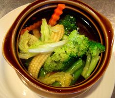 a brown bowl filled with broccoli and corn on top of a white plate