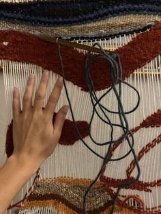 a hand is reaching for something on a rug that has been wovened with yarn