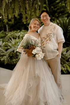 a man and woman standing next to each other in front of some trees with flowers