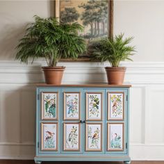 two potted plants sit on top of an old dresser with pictures painted on it