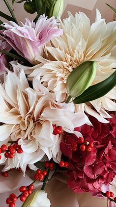 a bouquet of flowers with red berries on the bottom and green leaves in the middle