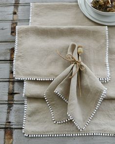 two linen napkins with beaded edges on a wooden table next to a white bowl