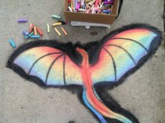 a box of crayons sitting on the ground next to a drawing of a dragon