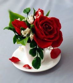 a red rose sitting on top of a saucer filled with white flowers and greenery