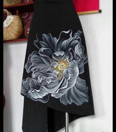 a black skirt with white flowers painted on the front and back, hanging from a wall