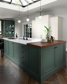 a kitchen with green cabinets and wooden counter tops, an island in the middle has a potted plant on it