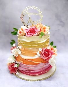 a multi layer cake with flowers and leaves on the top is decorated with gold lettering