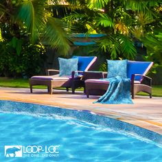 two lounge chairs sitting next to a swimming pool with palm trees in the back ground