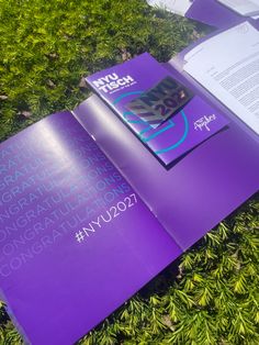 an open purple book sitting on top of green grass