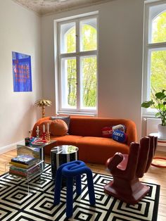 a living room with an orange couch and two chairs in front of large windows on the wall