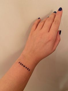 a woman's hand with a small tattoo on her left wrist that says forward