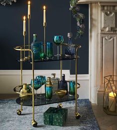 a table with candles and green glassware on it in front of a fire place