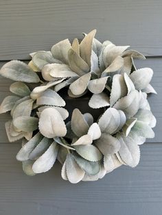 a white wreath hanging on the side of a gray wooden door with green and white leaves