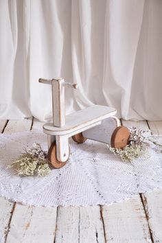 a wooden toy with wheels and flowers on a white doily covered floor next to a curtain