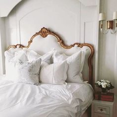 a white bed topped with lots of pillows next to a night stand and nightstands