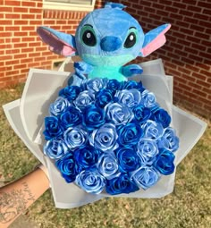 someone holding a bouquet of blue roses in front of a brick building with a tattoo on their arm