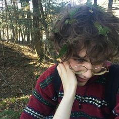 a young man with glasses sitting in the woods